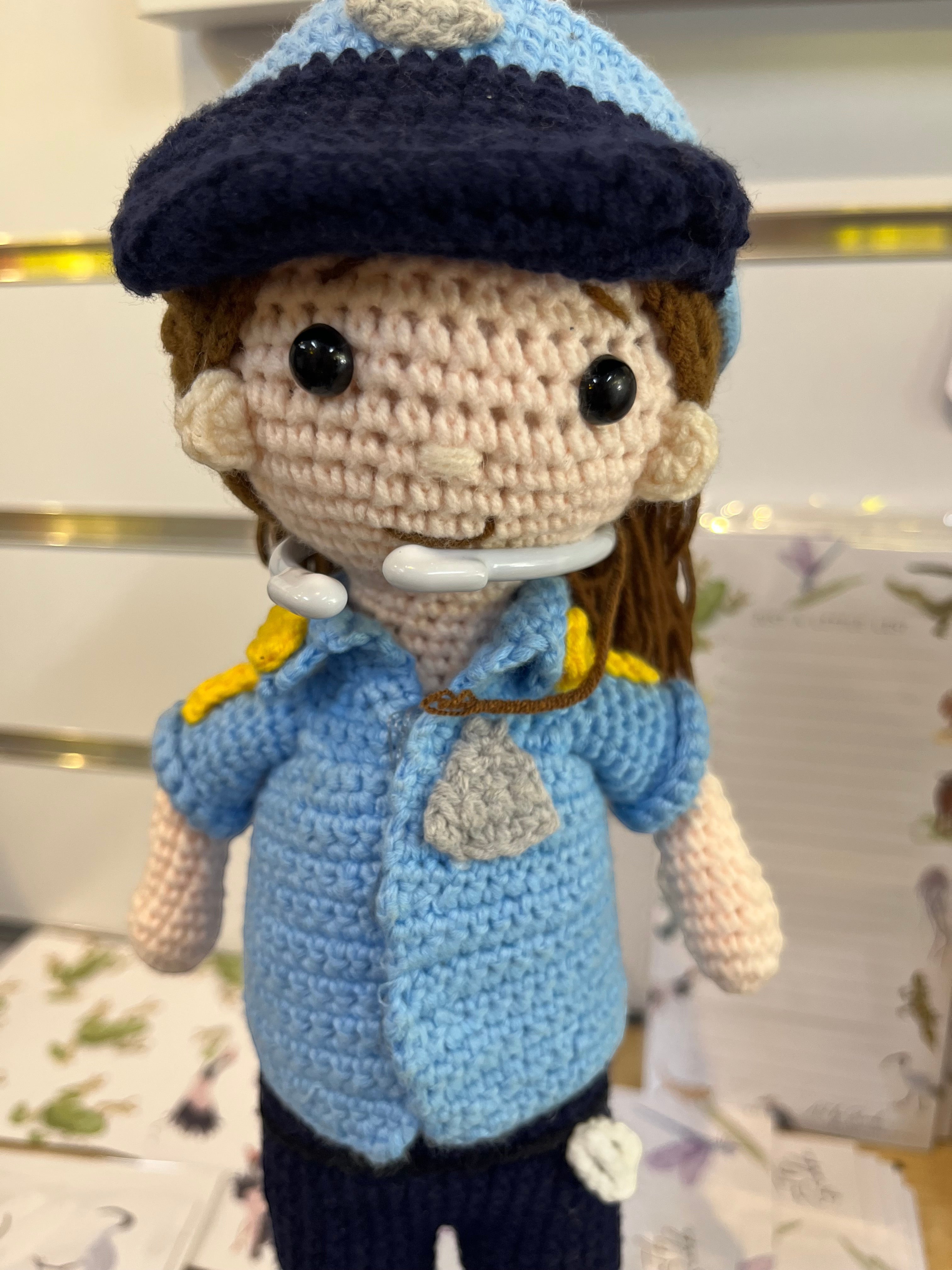 Suzie's Sunshine Dolls crocheted police officer doll in blue uniform with cap, badge, and yellow shoulder details.