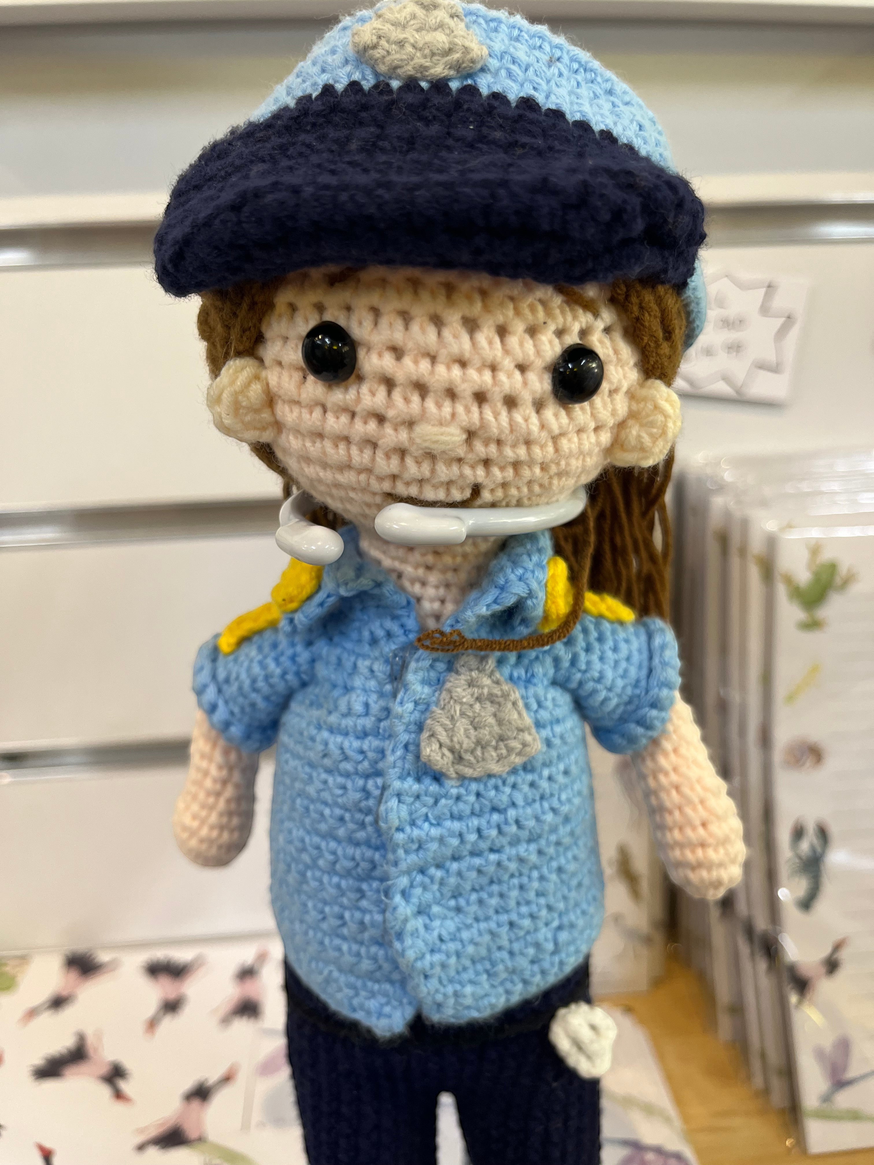 Suzie's Sunshine Dolls Policeman doll in blue uniform with navy cap, badge, and yellow accents. Handcrafted yarn toy.