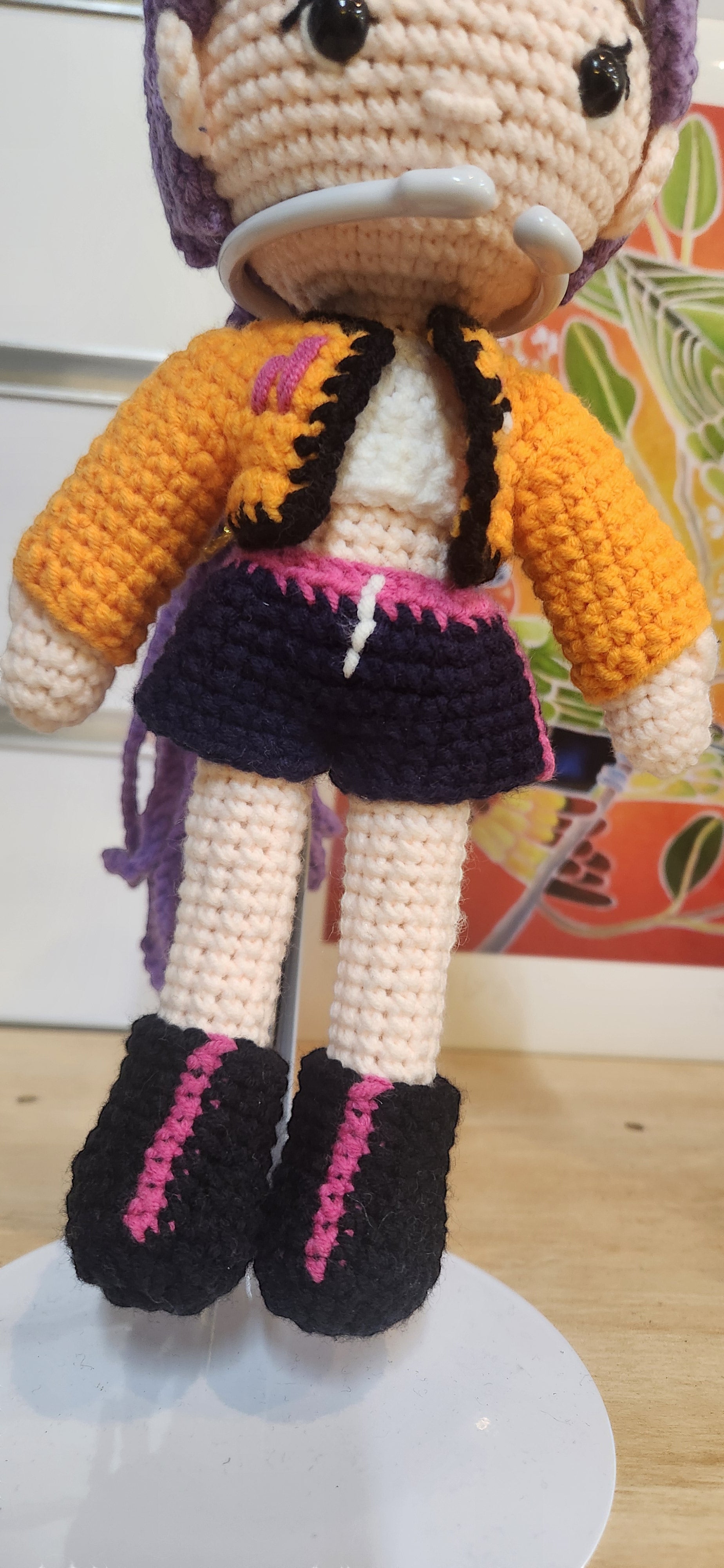 Suzie's Sunshine Dolls Rumi K-Pop Demon Hunter amigurumi doll with purple hair, orange jacket, and dark blue shorts.