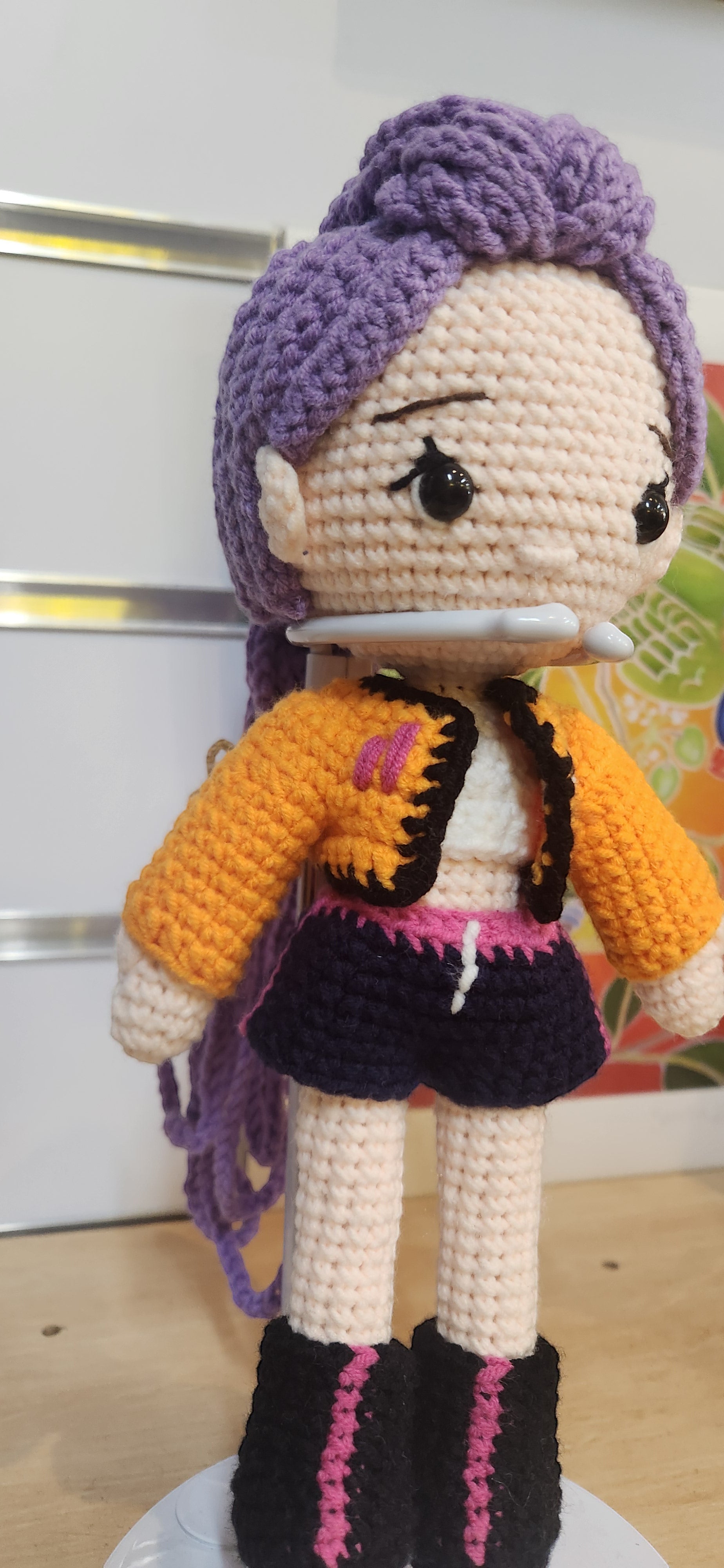 Suzie's Sunshine Dolls Rumi K-Pop Demon Hunter amigurumi doll with purple hair, orange jacket, and dark shorts.