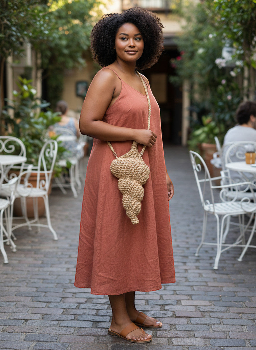 Suzie's Sunshine Dolls natural woven seashell shaped shoulder bag with braided strap, worn by a woman in a rust-colored dress.