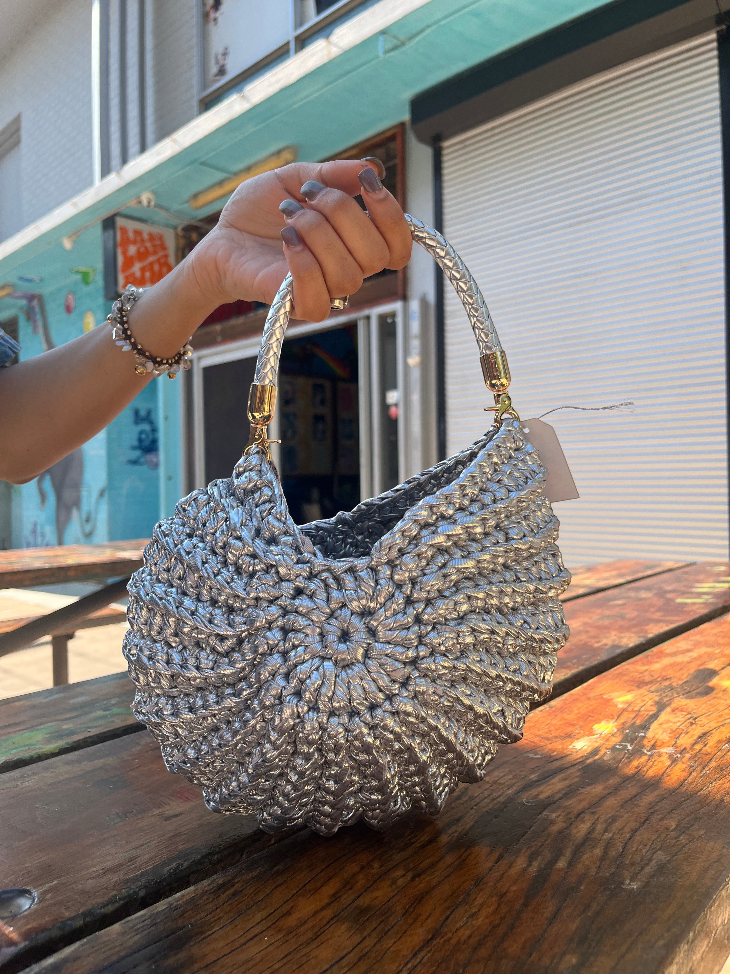 Suzie's Sunshine Dolls silver crochet shoulder bag with braided handle and textured crescent shape.