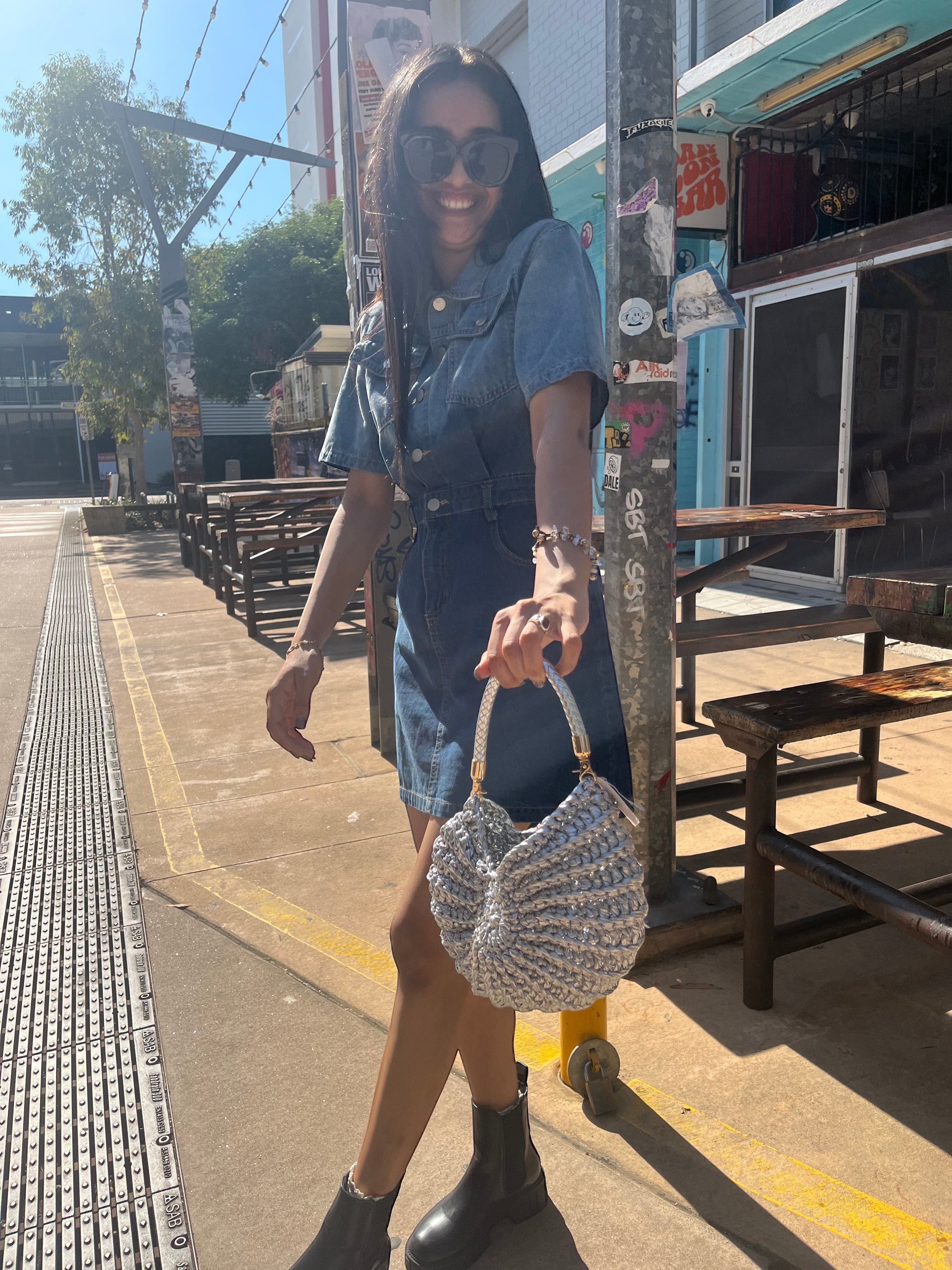 Suzie's Sunshine Dolls silver crochet shoulder bag with braided handle, crescent shape, textured detail.