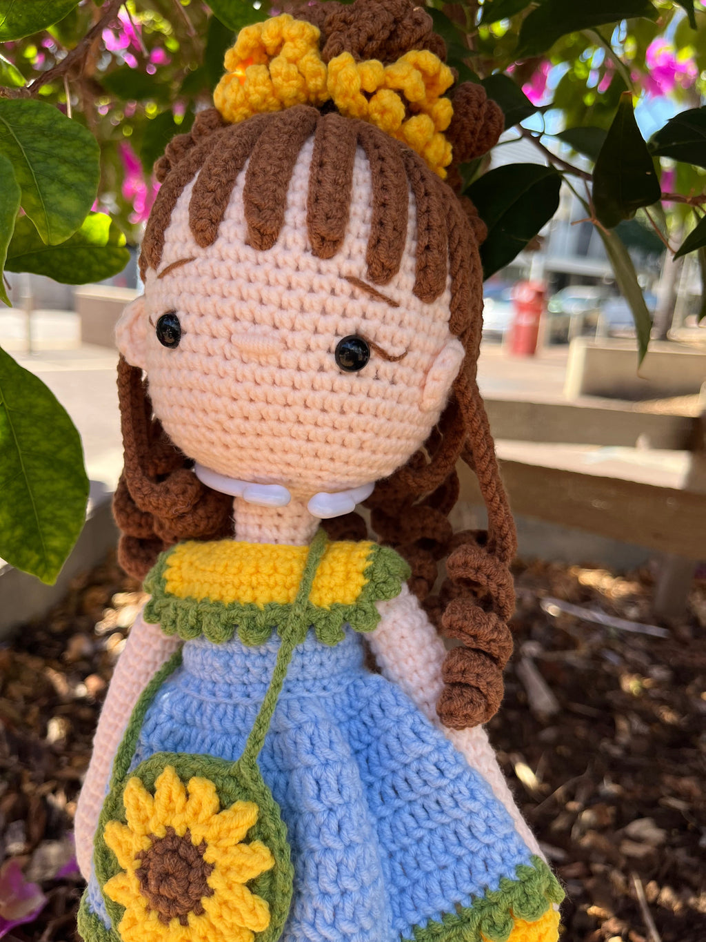 Suzie's Sunshine Dolls Sophie, a crochet doll with brown yarn hair, wearing a blue dress with yellow and green trim, and a sunflower purse.