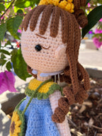 Suzie's Sunshine Dolls Sophie, a crocheted doll with brown yarn hair, wearing a blue dress with yellow and green trim, and a sunflower purse.