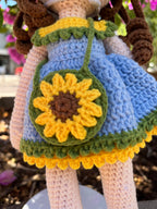 Suzie's Sunshine Dolls Sophie, a crocheted doll in a blue dress with yellow and green trim, holding a sunflower purse and wearing a flower crown.
