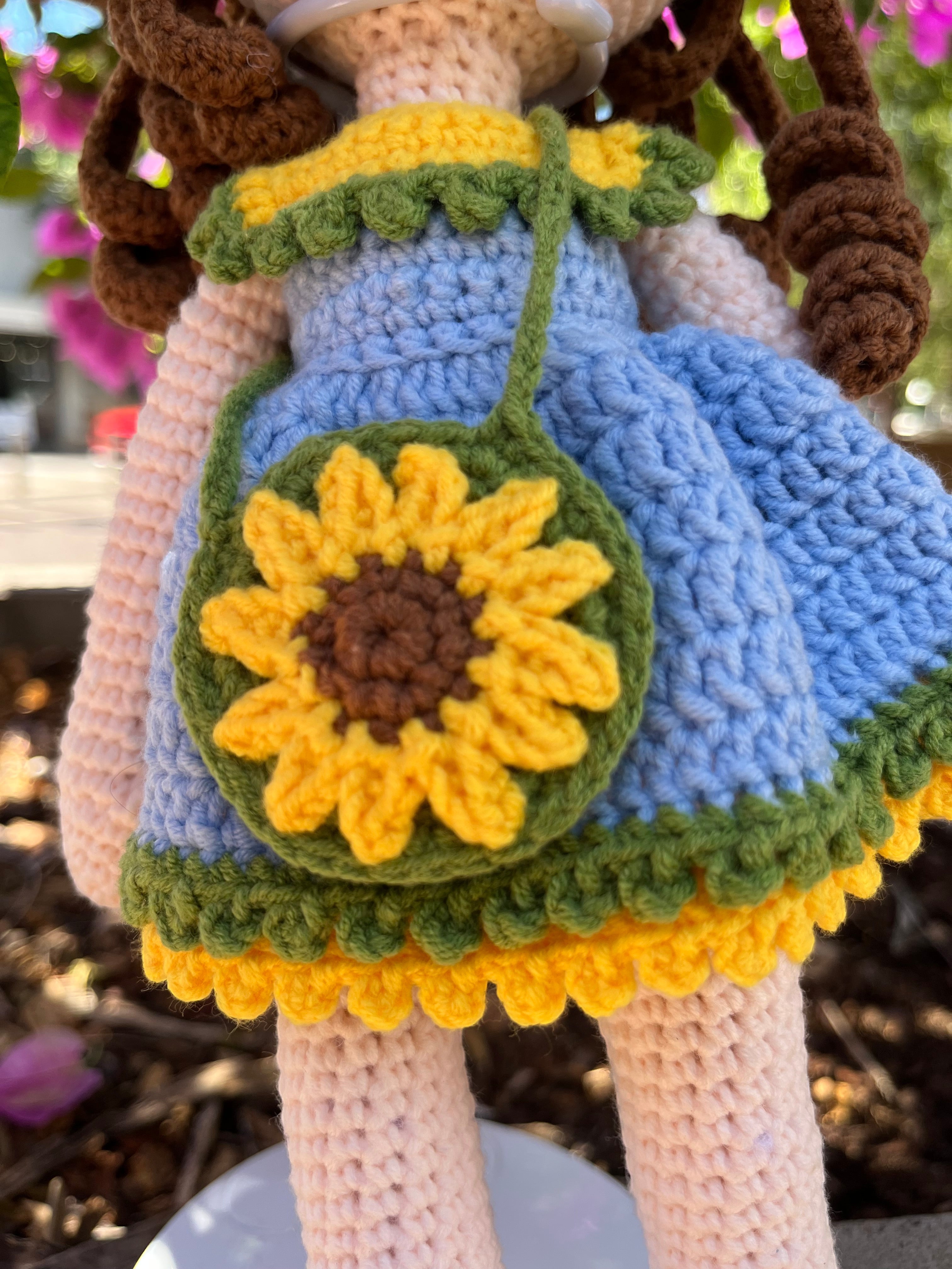 Suzie's Sunshine Dolls Sophie, a crocheted doll in a blue dress with yellow and green trim, holding a sunflower purse and wearing a flower crown.