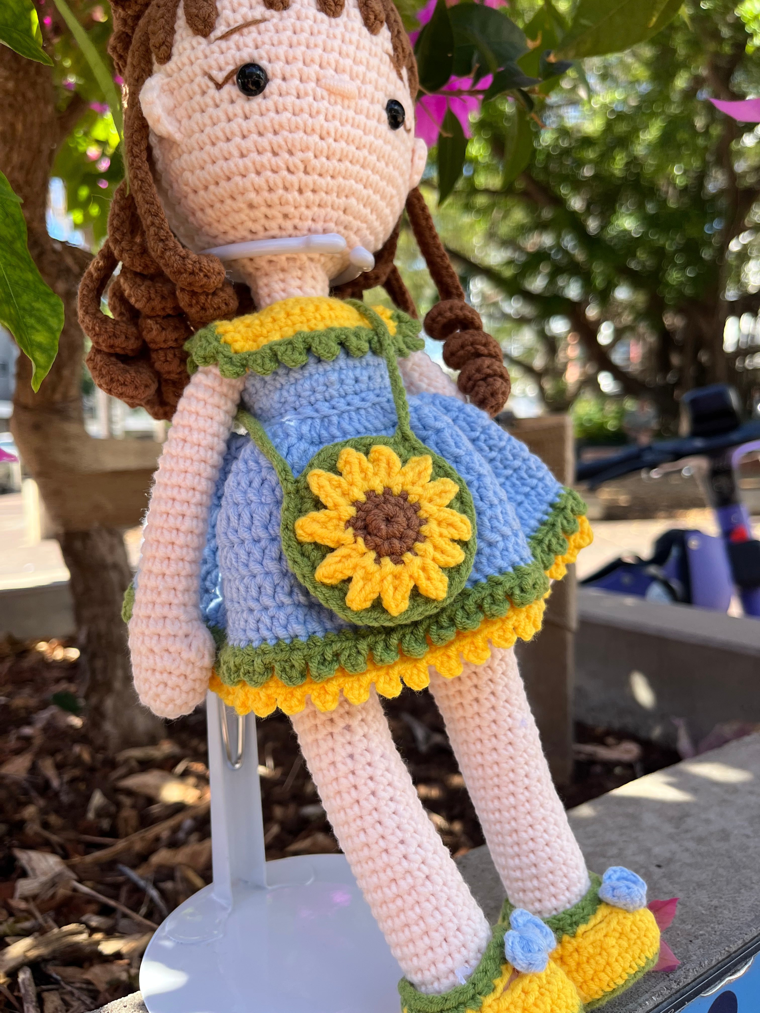 Suzie's Sunshine Dolls Sophie, a crocheted doll in a blue dress with yellow and green trim, holding a sunflower purse and wearing a flower crown.
