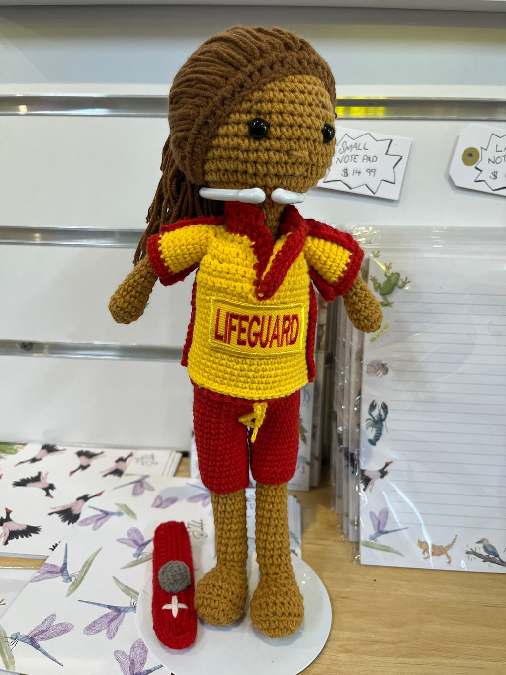 Suzie's Sunshine Dolls Surf Lifesaver doll, crocheted in red and yellow uniform with "LIFEGUARD" text and rescue float accessory.