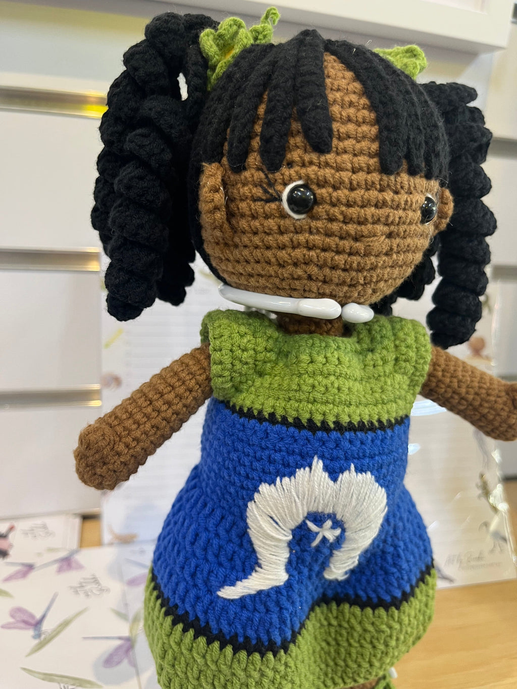 Suzie's Sunshine Dolls handmade crochet doll with long black curly hair, wearing a green and blue dress with white embroidery representing the Torres Strait Islander flag.
