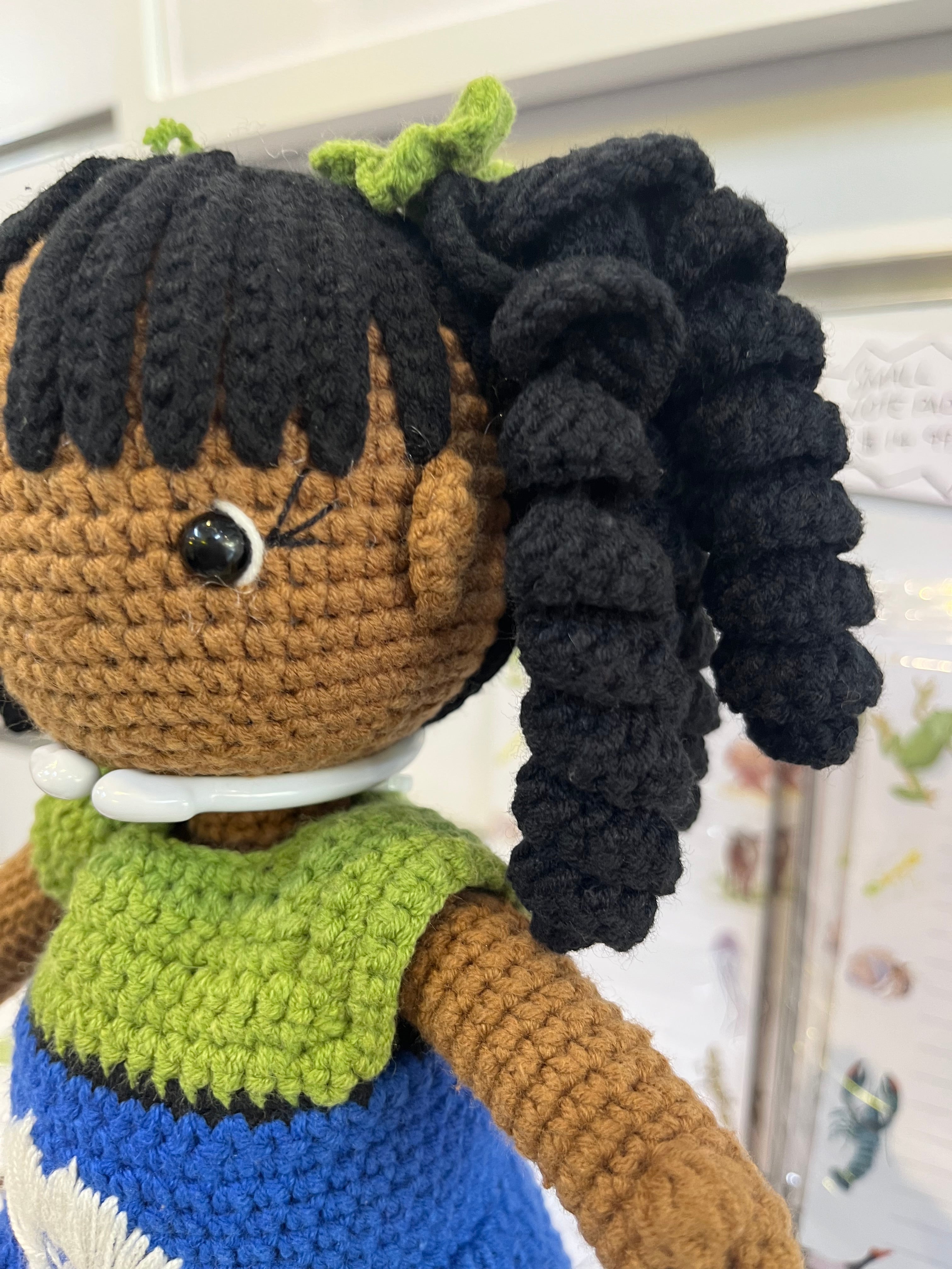 Suzie's Sunshine Dolls handmade crochet doll with long black curly hair and a Torres Strait Islander flag dress in blue and green.